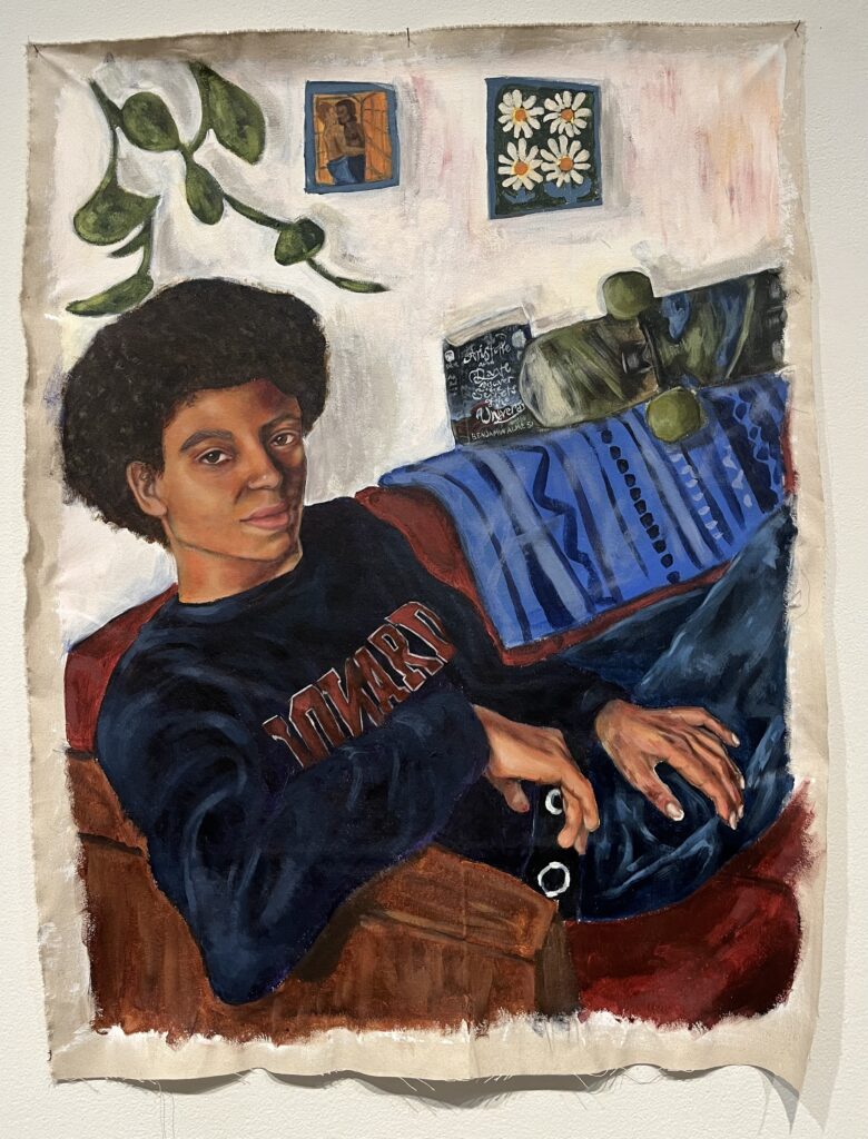 A Black person sits on a red couch leaning back with his head turned towards the viewer. He is wearing a navy Howard crewneck, a black belt with metal rings, and medium wash jeans. There is a blue patterned blanket draped over the couch and a book and skateboard sitting on top of the couch. A plant hangs in the upper left corner. A poster of four dasies hangs on the wall as well as a poster of two men kissing.