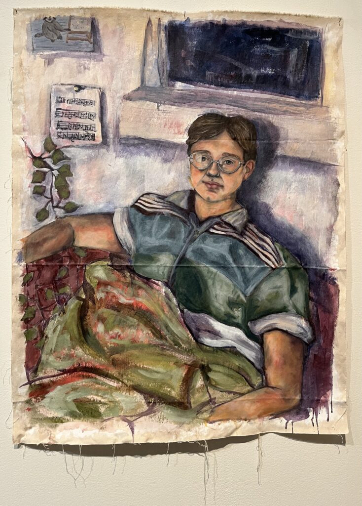 A white person wearing glasses sits on a red couch chair turned 3/4 towards the viewer. They are wearing a green and blue button down and have a green blanket draped over them. They are sitting under a dark window. There is a string of ivy coming from the left side. There is a page of music hanging up on the left side of the painting and a hand drawn birthday card on the top left.